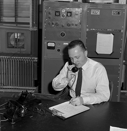 Man talking on telephone while writing at a desk in WERS studio